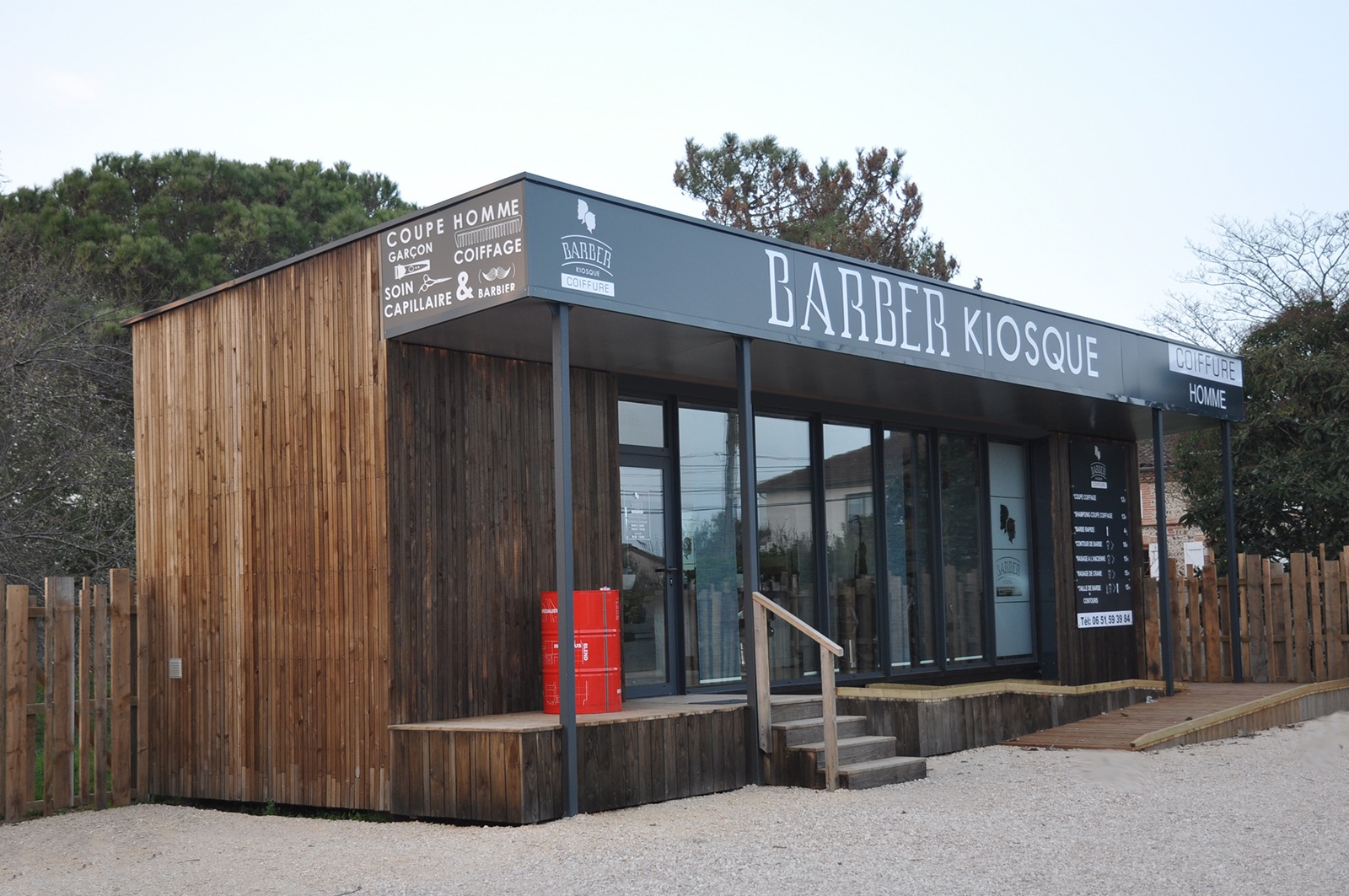 Salon de coiffure-Barber créé à partir d'un contener maritime. Bardage en bois brut grisé, coursive couverte et grande vitrine constitue une apparence modernisée de "saloon" de western.
