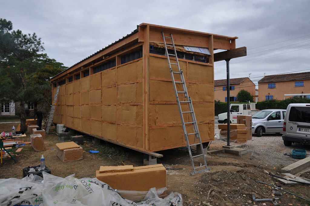 Salon de coiffure-Barber créé à partir d'un conteneur maritime. Le container est habillé d'une ossature secondaire en bois et rempli d'un isolant avant de recevoir un bardage en bois. Le tout supporte un toit rehaussé pour l'isolation et constituant une avancé supportée par une grande poutre en bois sur poteau d'acier.