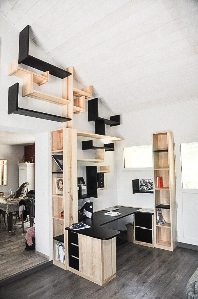 La Bibliothèque-Arbre associe un bureau, des éléments de rangement et un ensemble d'étagères suspendues dans une composition évoquant la silhouette d’un arbre. Alexandre Drabzak imagine ce mobilier comme une œuvre fonctionnelle, où les modules de bois clairs et noirs créent un jeu de branches et de ramures jouant avec le lumière