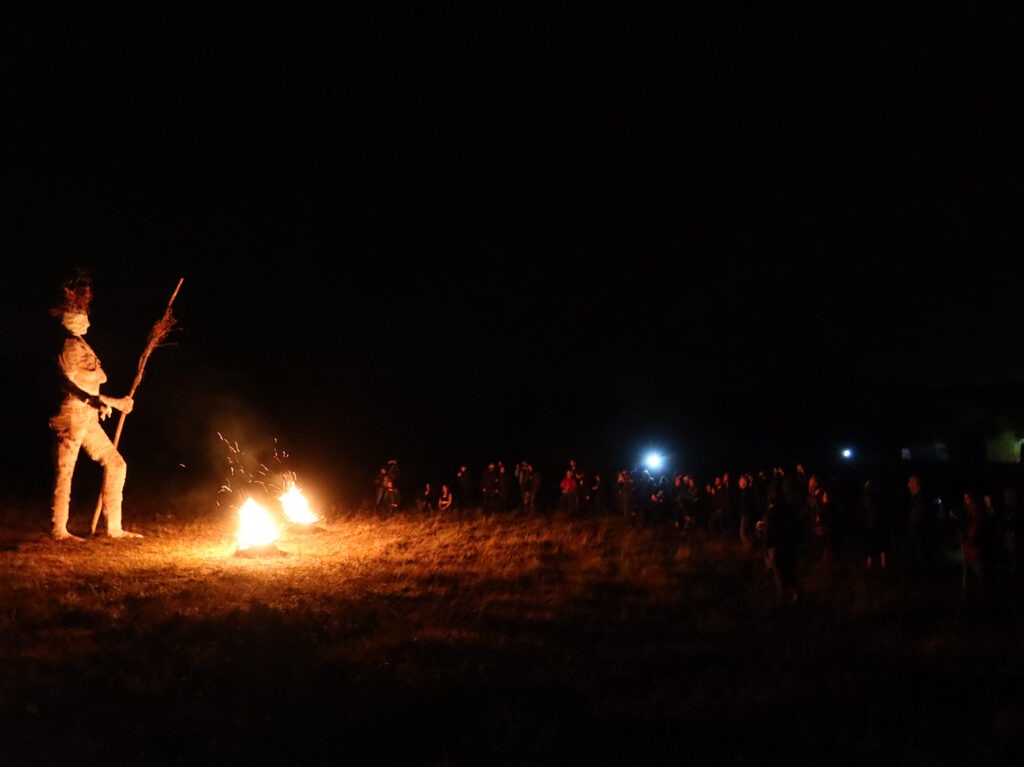 Photographie de nuit de la Pèlerine lors de la cérémonie de clôture de l'événement, devant brasero et grand public.