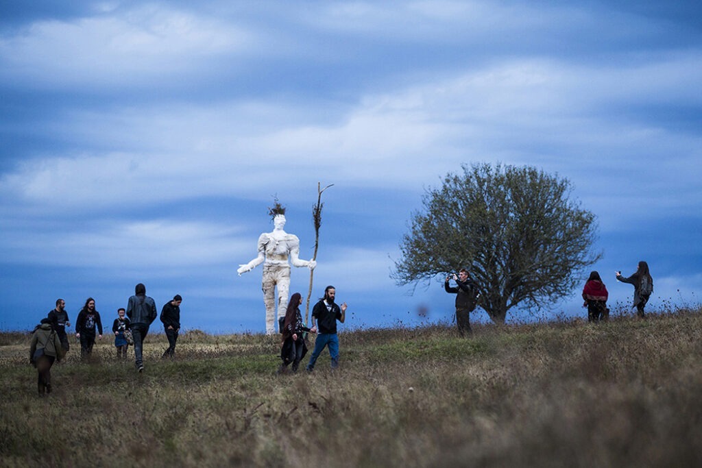 Photographie de la Pèlerine (sculpture de femme de 5m30) sur fond de ciel bleu avec en avant-plan le public de l'événement musical l'Homme sauvage.