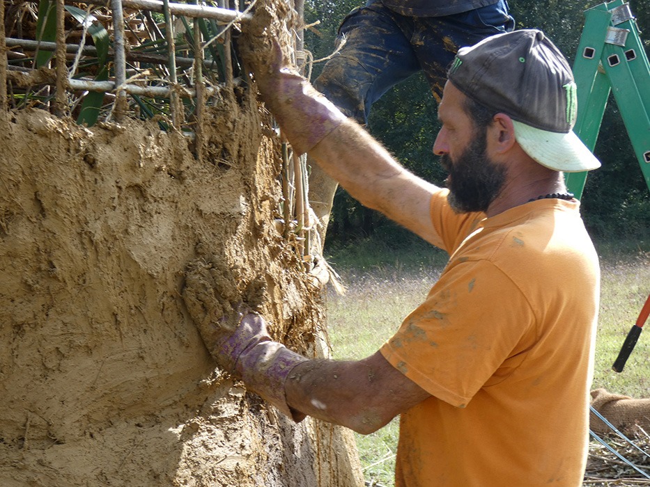 Photographie d'Alexandre Drabzak travaillant à installer le torchis de terre cru constituant le corps de la Vénus monumentale lors de l'événement musical l'homme sauvage 2024.