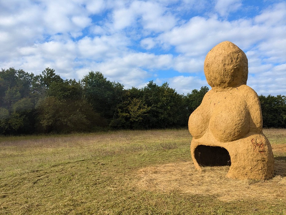 Photographie de la Vénus monumentale en terre cru, à son premier jour, dans un décors de prairie et de bois, créée à l'occasion de l'événement musical l'homme sauvage 2024 par Alexandre Drabzak.