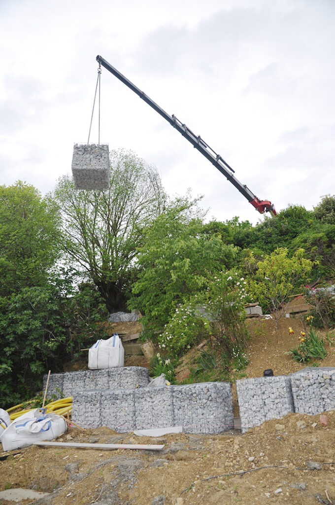 Photographie montrant l'installation des gabions de soutènement au moyen d'une grue de grande dimension.