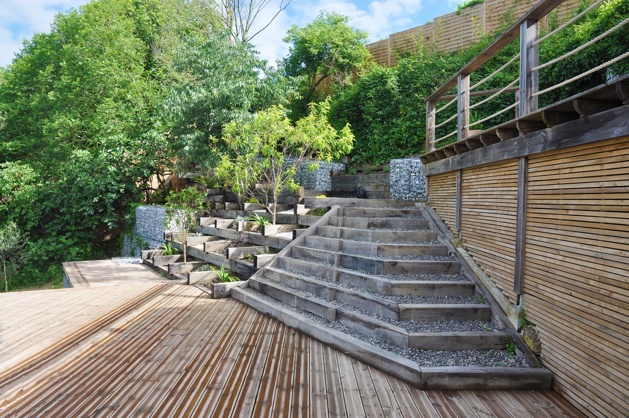 Photographie d'un escalier de jardin rappelant les marches d'un temple ancien, constituant le lien entre le niveau haut (chemin d'accès, pool-house et terrasse bois) et le niveau intermédiaire (grande terrasse en bois) de l'espace.
