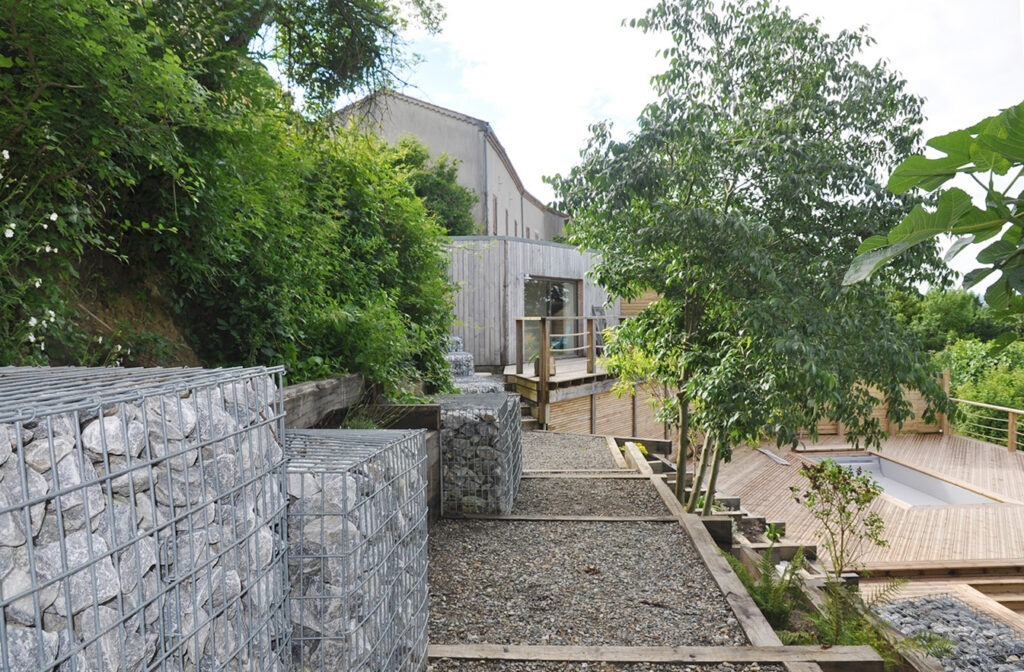 Photographie d'ensemble de l'aménagement avec en fond le pool house, la une grande terrasse avec piscine et le chemin aménagé qui permet d'y accéder. 