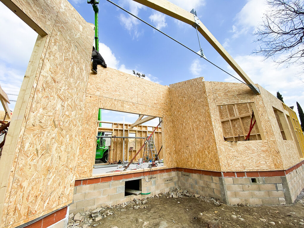Photographie prise depuis l'extérieure au moment des travaux montrant une alcôve, une charpente moderne mêlant bois et métal, les murs en ossature bois, et les futures ouvertures.