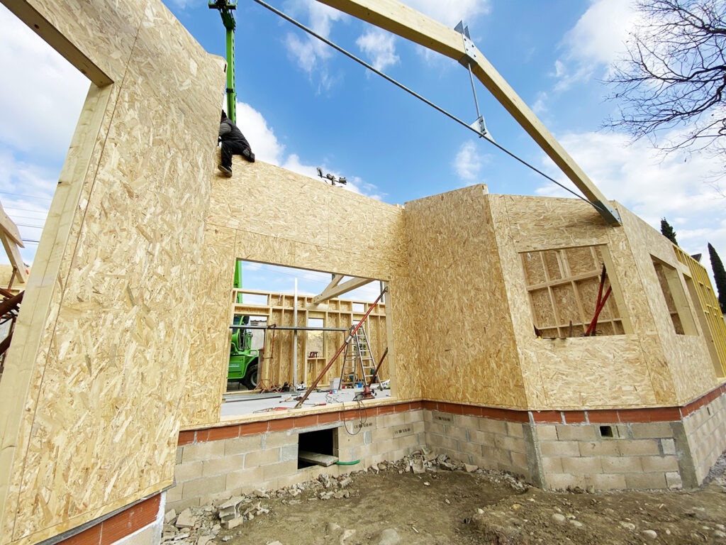 Photographie prise depuis l'extérieure au moment des travaux montrant une alcôve, une charpente moderne mêlant bois et métal, les murs en ossature bois, et les futures ouvertures.