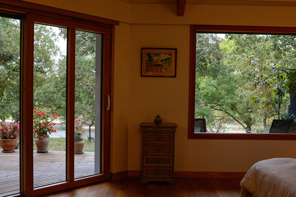 Photographie de la grande baie fixe et baie vitrée coulissante en bois de la chambre principale, donnant sur le fleuve Garonne.
