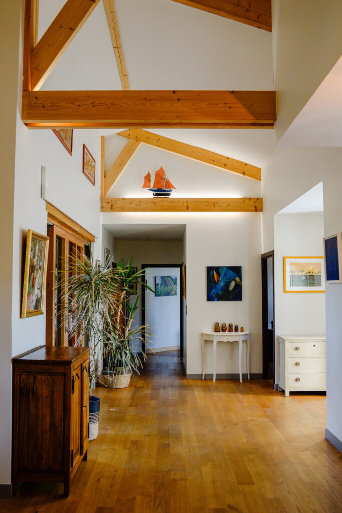 Photographie de la charpente apparente encadrant la grande entrée avec grande baie vitrée donnant vue sur le fleuve et couloir desservant les chambres et la salle de bain.