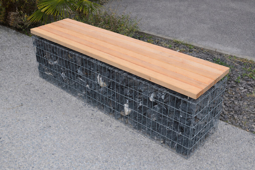 Banc-Gabion constitué d'une assise en bois fixée sur un gabion (cage de métal rempli de pierre), installé devant les locaux d'OMG.
