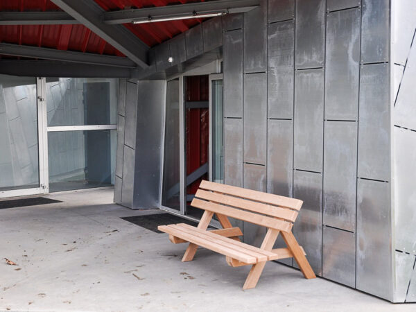 Banc en bois design installé devant un édifice moderne couvert de plaque de métal.