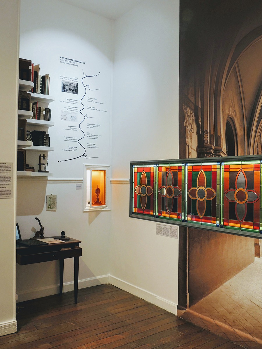 Photographie en perspective du musée montrant le petit bureau de Marie-Eugénie avec des livres anciens, une partie de la frise historique, une partie de la grande photographie de l'ancien cloître et le vitrail découvert lors des travaux.