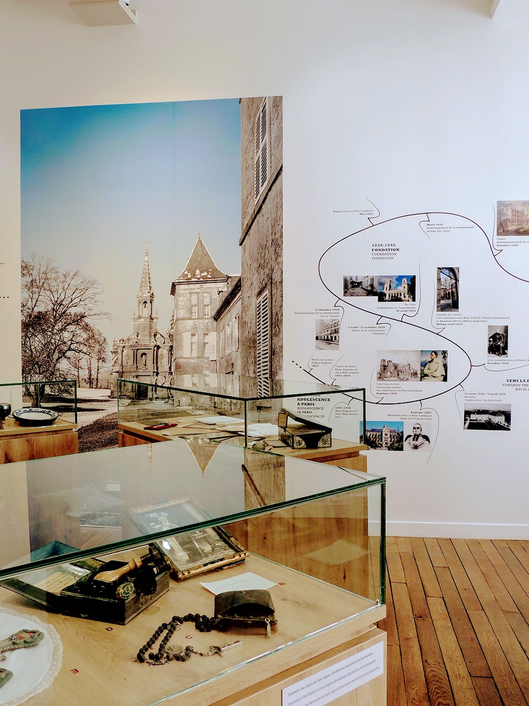 Photographie en perspective du musée montrant plusieurs vitrine d'objets de souvenirs, la seconde partie de la frise historique et la grande photographie du Château de Preisch (Lorraine) et sa chapelle.