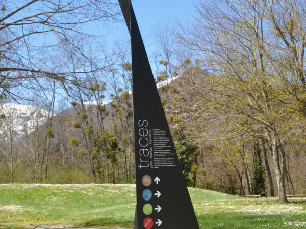 Photographie d'un totem design, en acier plié et thermolaqué, en cohérence avec l'architecture contemporaine marquée du site. Le principe design n'est pas sans rappeler les origamis. Celui-ci, destiné à marquer et informer un lieu d'exposition ou d'animation extérieur, comprend le nom et la description de l'atelier, ainsi que des symboles directionnels.