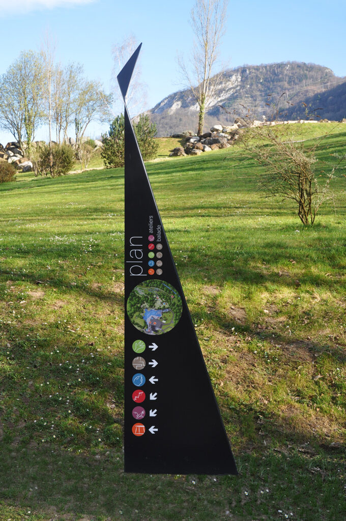 Photographie d'un totem design, en acier plié et thermolaqué, en cohérence avec l'architecture contemporaine marquée du site. Le principe design n'est pas sans rappeler les origamis. Celui-ci comprend un plan du site et des symboles directionnels.