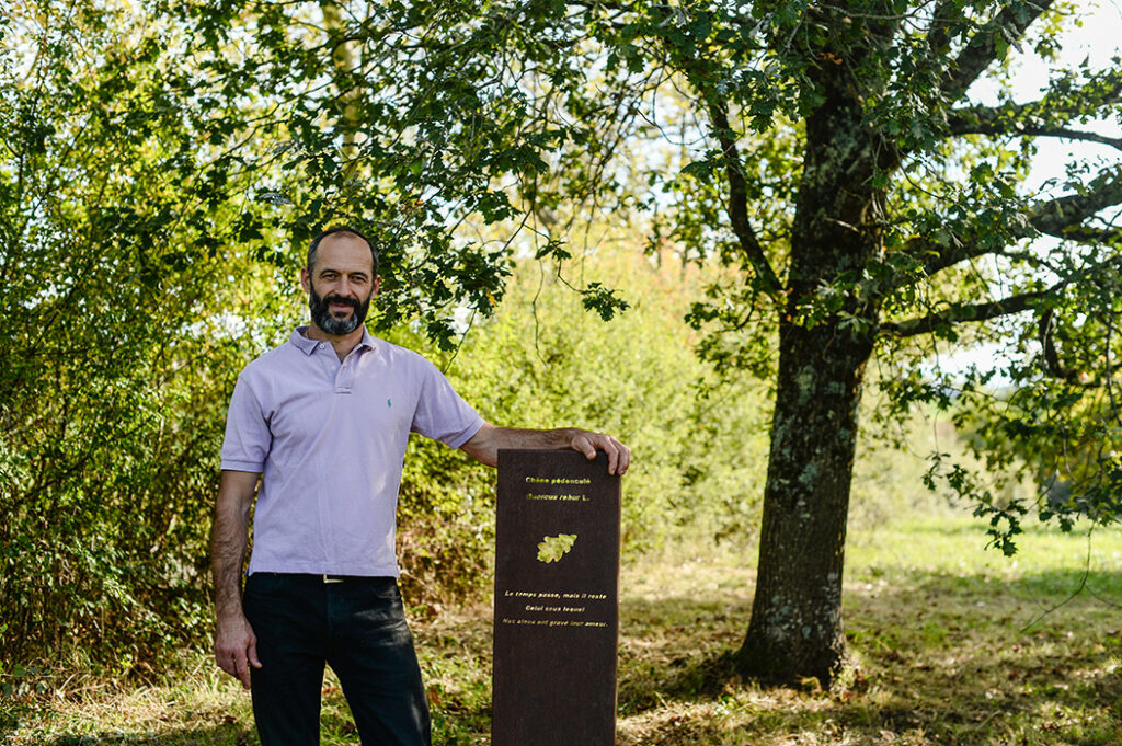 Photographie d'une stèle botanique et poétique en acier Corten dédié au Chêne pédonculé, devant son sujet et avec son créateur Alexandre Drabzak.