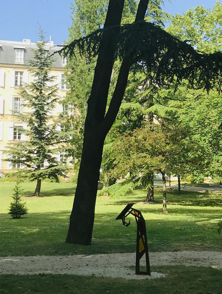 Photographie d'un lutrin implanté au cœur du parc arboré du Couvent des Sœur de l'Assomption. En fond, le bâtiment principal du couvent. La forme du lutrin inspiré du végétal (crosse de fougère) trouve ici tout son sens. Design et concept par Alexandre Drabzak.
