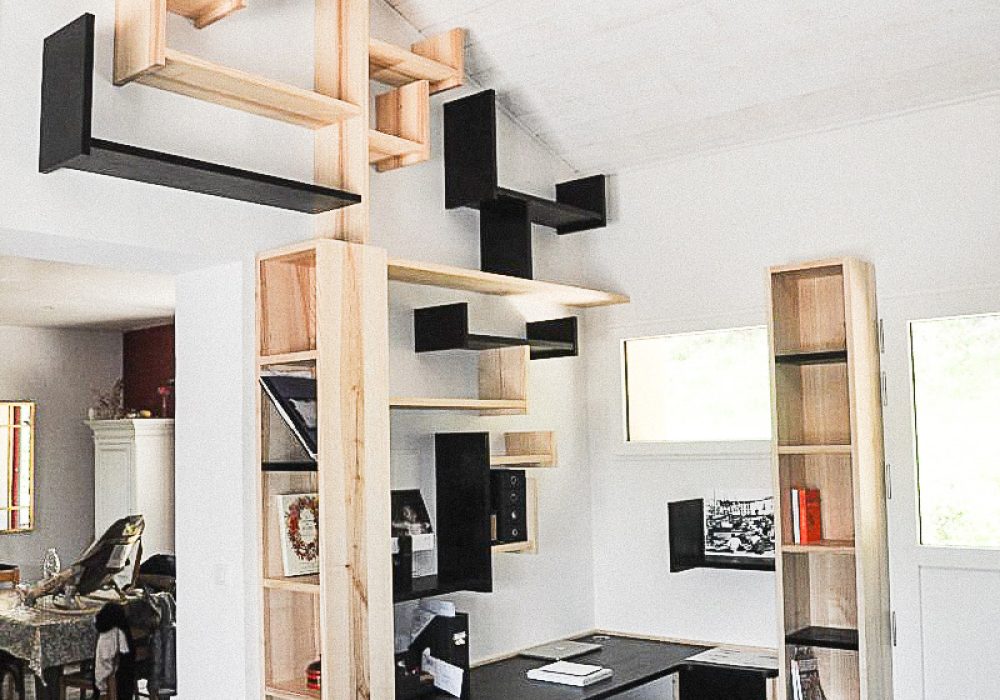 La Bibliothèque-Arbre associe un bureau, des éléments de rangement et un ensemble d'étagères suspendues dans une composition évoquant la silhouette d’un arbre. Alexandre Drabzak imagine ce mobilier comme une œuvre fonctionnelle, où les modules de bois clairs et noirs créent un jeu de branches et de ramures jouant avec le lumière