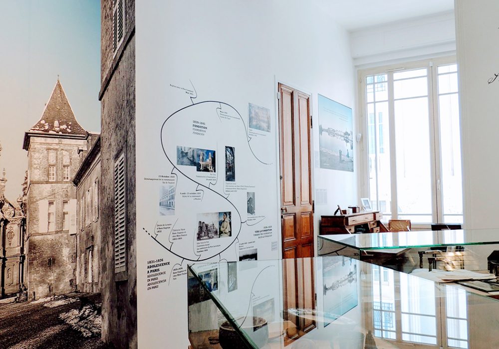 Photographie en perspective du musée montrant plusieurs vitrine d'objets de souvenirs, la seconde partie de la frise historique, une part de la grande photographie du Château de Preisch (Lorraine) et sa chapelle, et le bureau de Mère Thérèse-Emmanuel.