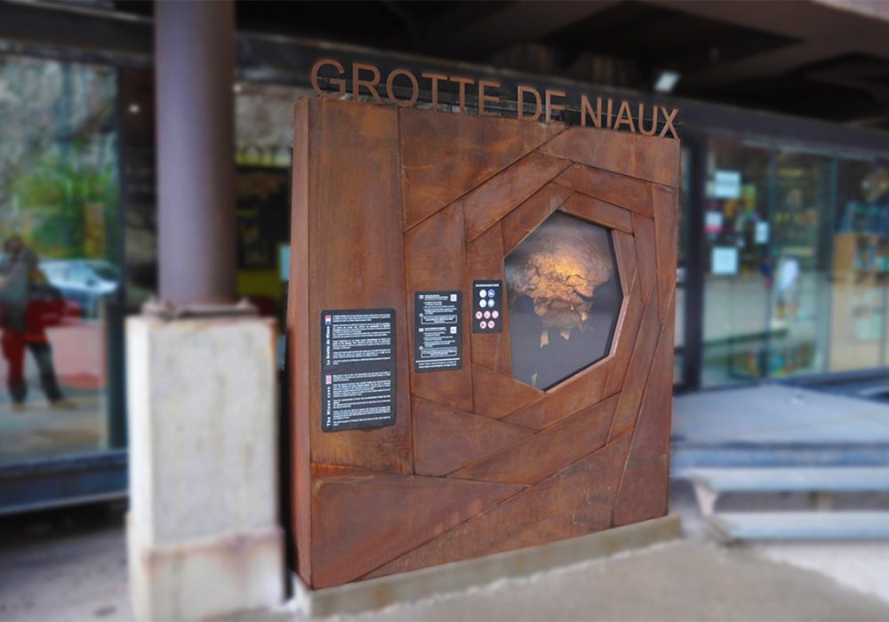Panneau d'accueil de la grotte de Niaux, pensé comme un support design attractif en cohérence matérielle avec l'arche de Massimiliano Fuksas qui marque de façon monumentale l'entrée de la Grotte. Le panneau destiné à recevoir les informations essentielles et préalable à la visite du site, est un grand carré constitué "d'écailles" en acier Corten dont les formes et l'assemblage symbolisent autant un principe d'obturateur photographique mécanique, comme un instantané en zoom sur le passé, qu'une métaphore de la caverne qui s'enfonce vers les profondeurs de la terre et du temps.